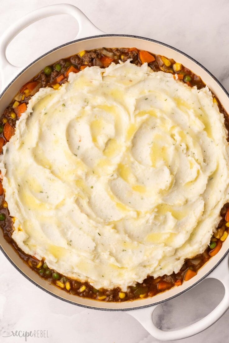 mashed potatoes spread over shepherds pie in white skillet.