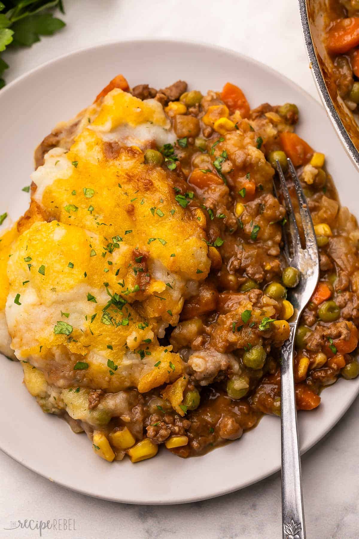grey plate filled with shepherds pie and a fork topped with chopped parsley.