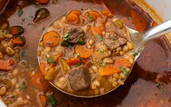 steel scoop full of beef barley soup in slow cooker.