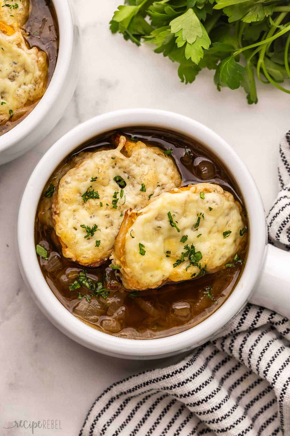 large white bowl of french onion soup with a towel beside.