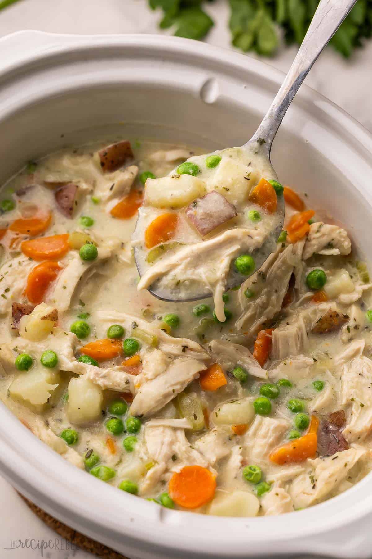 a spoon scooping garlic parmesan chicken stew out of white slow cooker.