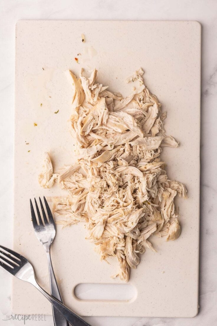 shredded chicken on a cutting board with two forks beside.