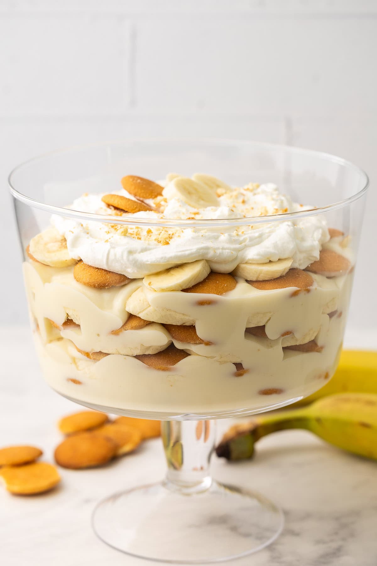 homemade banana pudding in a glass dessert bowl with wafer cookies and bananas.