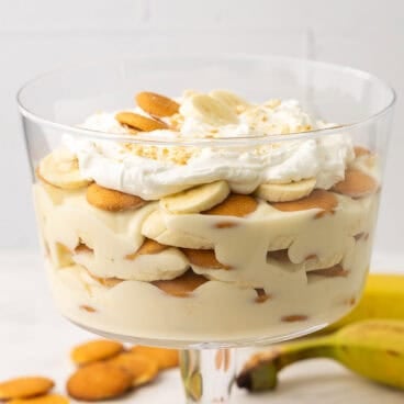 square image of banana pudding in glass dessert bowl with whipped cream.