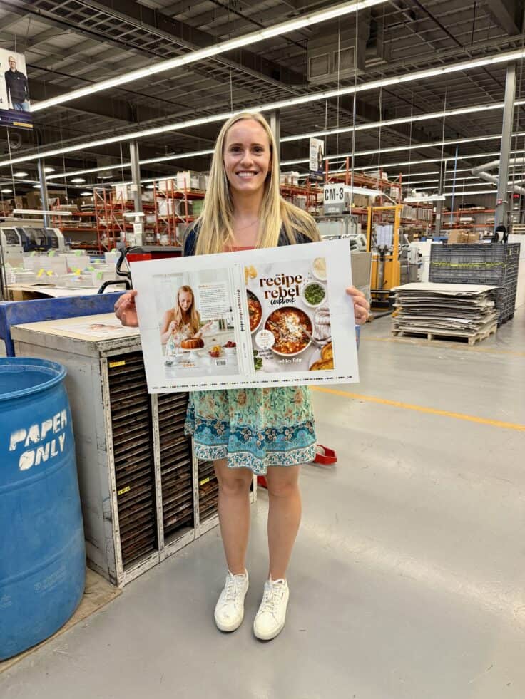 Ashley standing in print shop holding printed cookbook cover.
