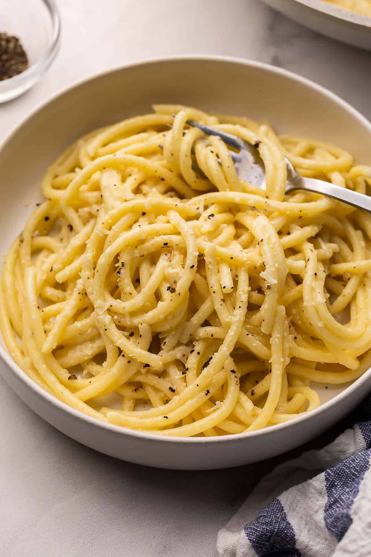 This 20-minute Cacio e Pepe recipe is creamy, peppery, and made with just 6 ingredients. Featuring al dente pasta, freshly grated Parmesan, and cracked black pepper, it's simple Italian comfort food at its best! #pasta #dinner | easy recipes | easy dinner recipes | pasta recipes | 20 minute meals | 30 minute meals | italian food | parmesan | cracked black pepper grey bowl filled with cacio e pepe and a fork.