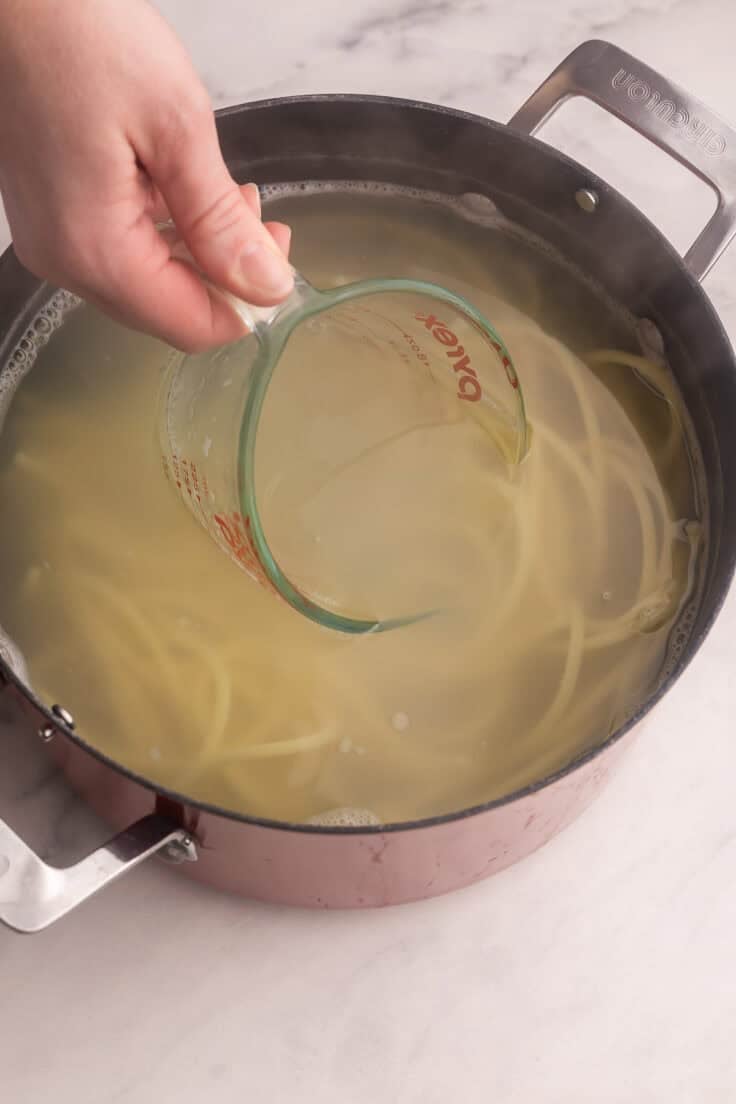 a measuring cup scooping pasta water from boiled pasta pot.