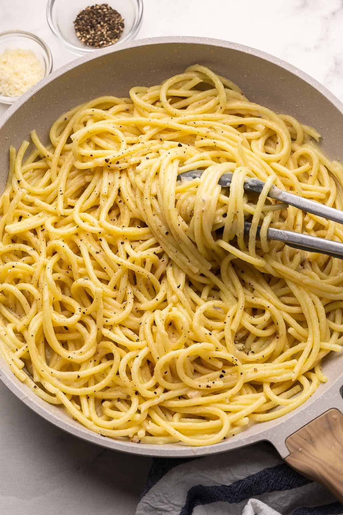 This 20-minute Cacio e Pepe recipe is creamy, peppery, and made with just 6 ingredients. Featuring al dente pasta, freshly grated Parmesan, and cracked black pepper, it's simple Italian comfort food at its best! #pasta #dinner | easy recipes | easy dinner recipes | pasta recipes | 20 minute meals | 30 minute meals | italian food | parmesan | cracked black pepper tongs grabbing cacio e pepe out of pan.