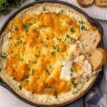chicken alfredo dip in a black skillet with bread beside.