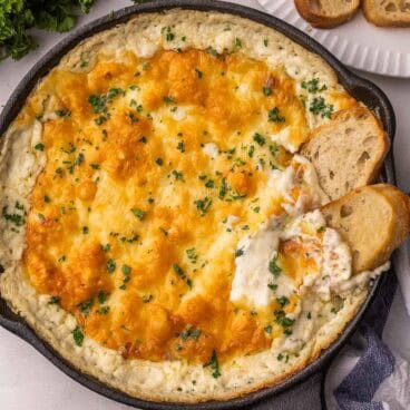 chicken alfredo dip in a black skillet with bread beside.