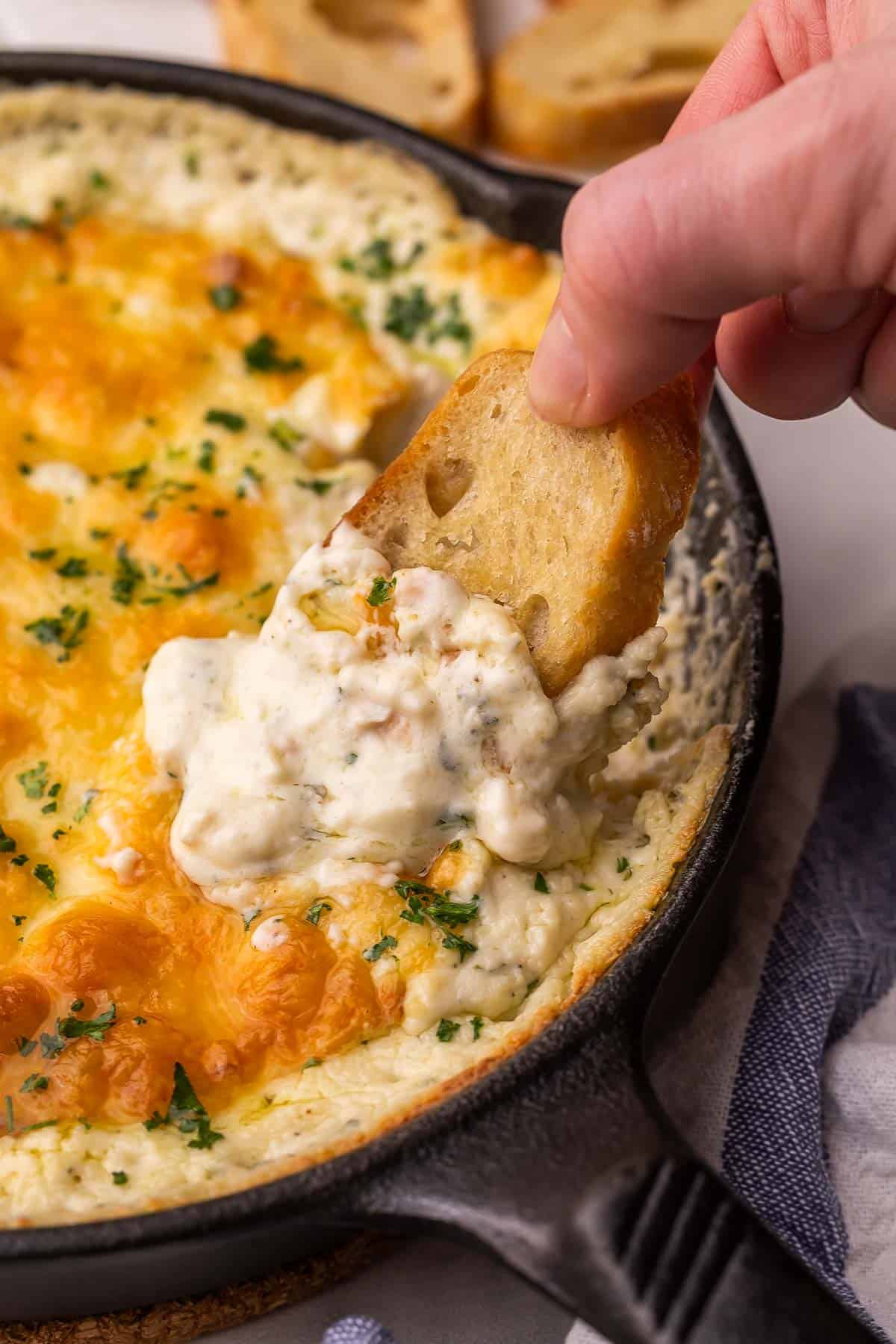 a hand dipping bread into chicken alfredo dip.