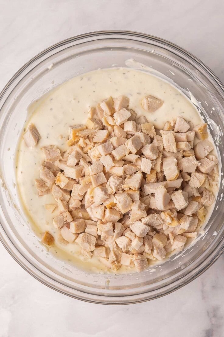 chopped chicken added to alfredo sauce in bowl.