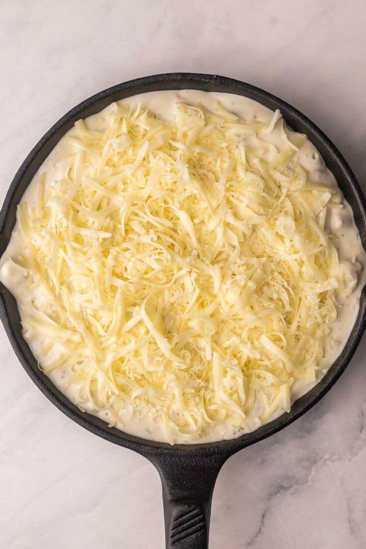 cheese added to top of skillet full of chicken alfredo dip.
