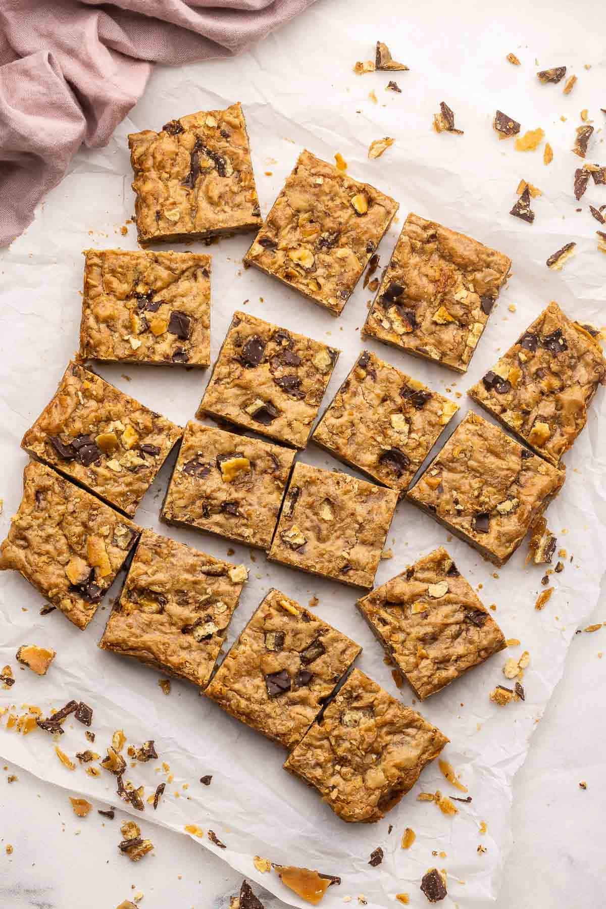 These Christmas Crack Blondies are chewy, buttery bars packed with caramel-chocolate cracker toffee. Made in just 45 minutes, they’re the perfect mash-up of two classic desserts! #dessert #recipe | dessert recipes | christmas recipes | christmas desserts | chocolate | caramel christmas crack blondies cut into pieces on parchment paper.