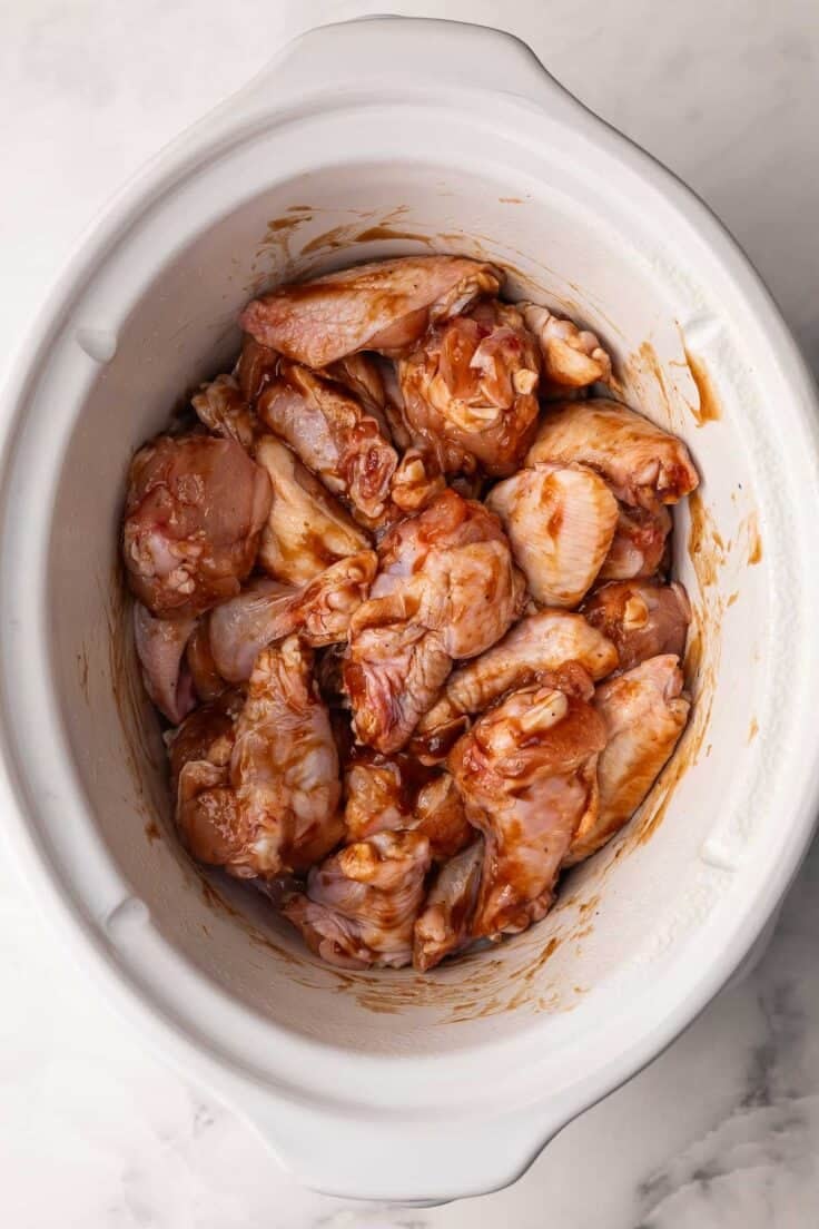 uncooked saucy chicken wings in white slow cooker.
