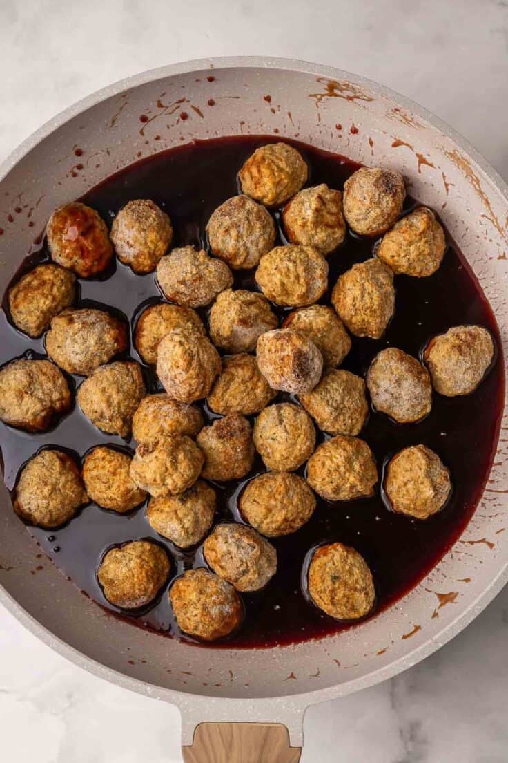 frozen meatballs added to sauce in frying pan.