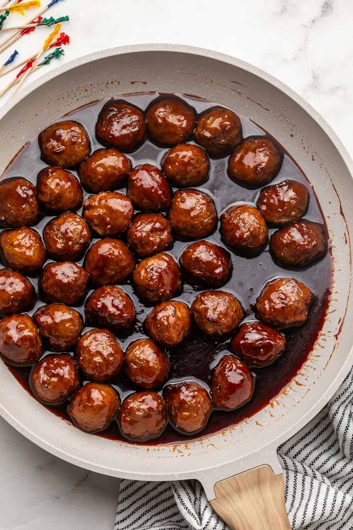 grey frying pan filled with grape jelly meatballs.