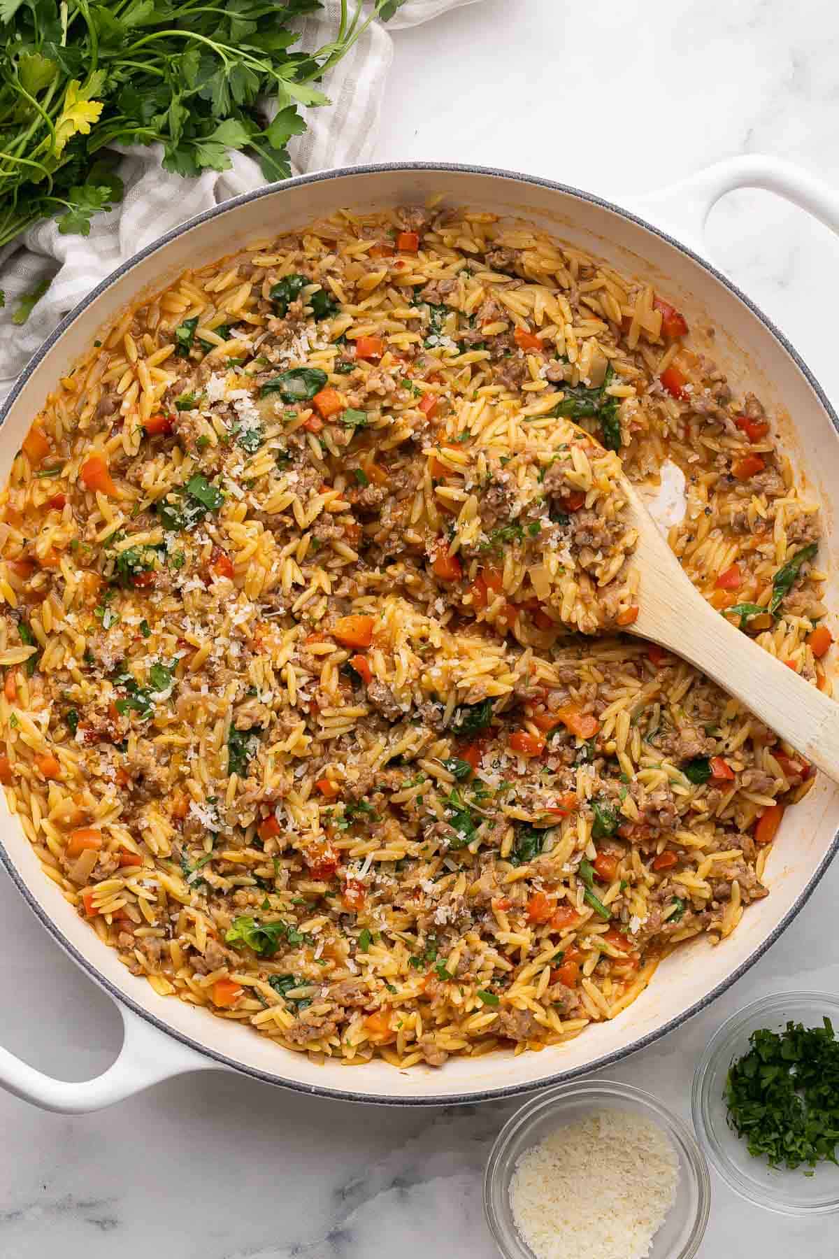 overhead image of italian sausage orzo pasta in white skillet with wooden spoon.