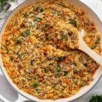 square image of italian sausage orzo in white braiser with wooden spoon stuck in.