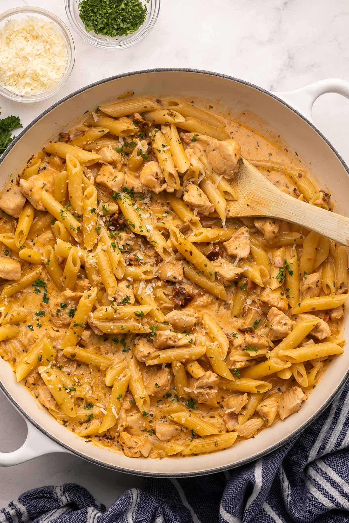 This One Pan Marry Me Chicken Pasta is packed with smoky bacon, juicy chicken breast, and nestled in a creamy sun-dried tomato sauce. It's a marriage proposal and cozy dinner all ready in 40 minutes that will make anyone say, "I do!" #pasta #recipe | dinner ideas | dinner recipes | one pan meal | one pot pasta | chicken breast recipes white skillet full of marry me chicken pasta with wooden ladle in it.