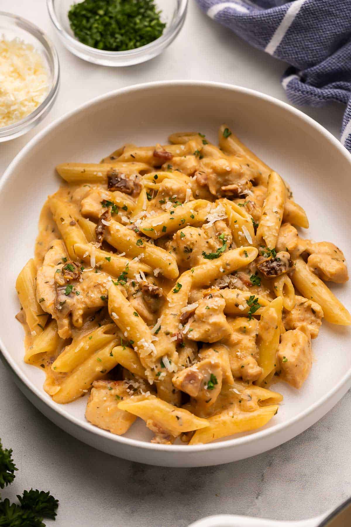 This One Pan Marry Me Chicken Pasta is packed with smoky bacon, juicy chicken breast, and nestled in a creamy sun-dried tomato sauce. It's a marriage proposal and cozy dinner all ready in 40 minutes that will make anyone say, "I do!" #pasta #recipe | dinner ideas | dinner recipes | one pan meal | one pot pasta | chicken breast recipes grey bowl filled with marry me chicken pasta with chopped parsley behind it.