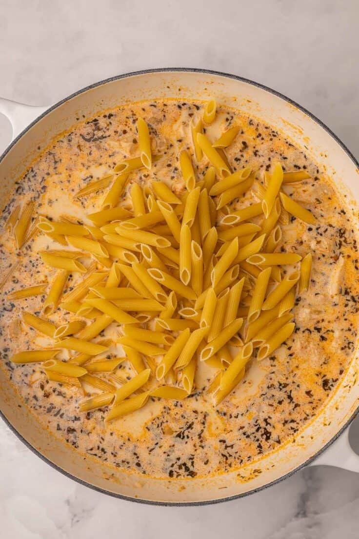 uncooked pasta added to sauce in white skillet.