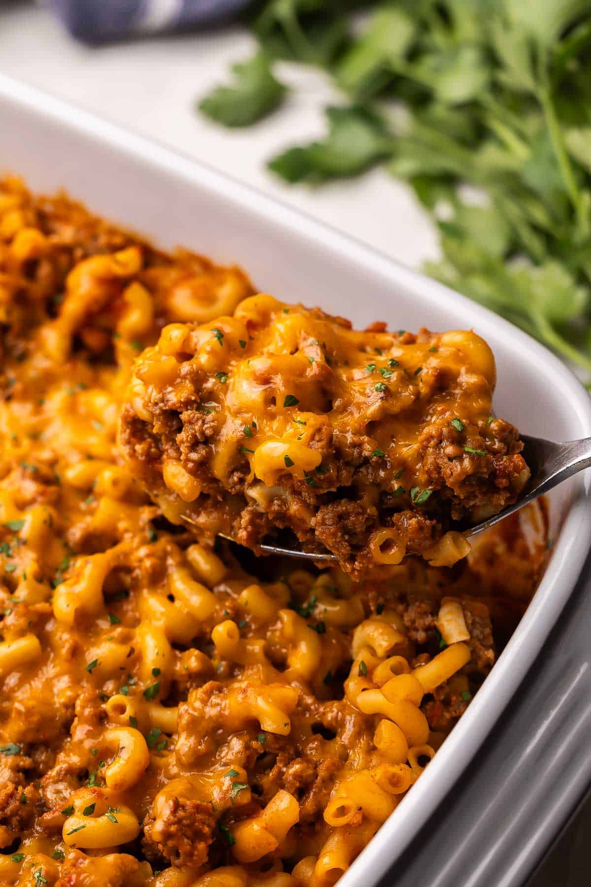 This cheesy No Boil Baked Cheeseburger Pasta is a 35-minute dinner winner! Everything cooks in one dish, which means no boiling, no browning, just cheesy, beefy goodness. #pasta #recipe #dinner | easy dinner ideas | dinner recipes | ground beef recipes | casseroles | make ahead meals | pasta bake scooping baked cheeseburger pasta out of pan.