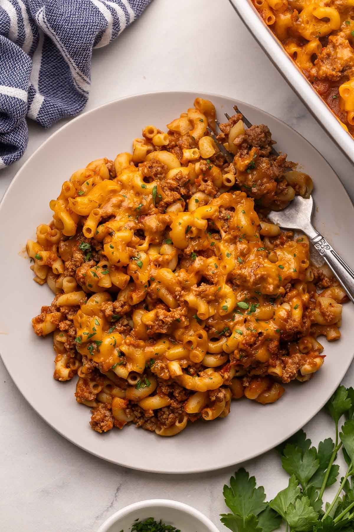 This cheesy No Boil Baked Cheeseburger Pasta is a 35-minute dinner winner! Everything cooks in one dish, which means no boiling, no browning, just cheesy, beefy goodness. #pasta #recipe #dinner | easy dinner ideas | dinner recipes | ground beef recipes | casseroles | make ahead meals | pasta bake a plate filled with baked cheeseburger pasta and a fork.