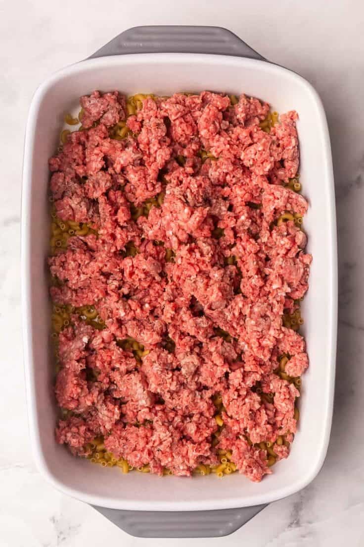ground beef added to dish of uncooked macaroni.