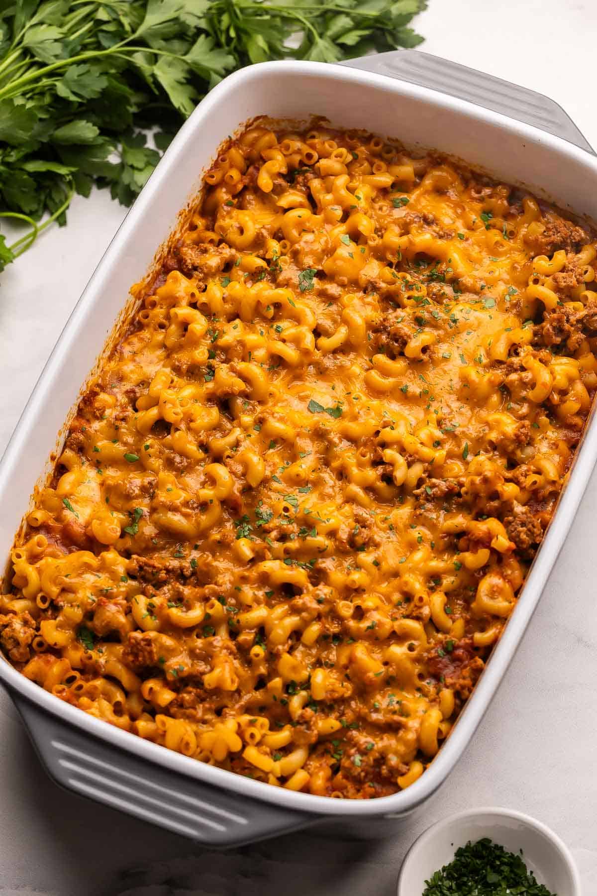 This cheesy No Boil Baked Cheeseburger Pasta is a 35-minute dinner winner! Everything cooks in one dish, which means no boiling, no browning, just cheesy, beefy goodness. #pasta #recipe #dinner | easy dinner ideas | dinner recipes | ground beef recipes | casseroles | make ahead meals | pasta bake large pan full of baked cheeseburger pasta with parsley beside.