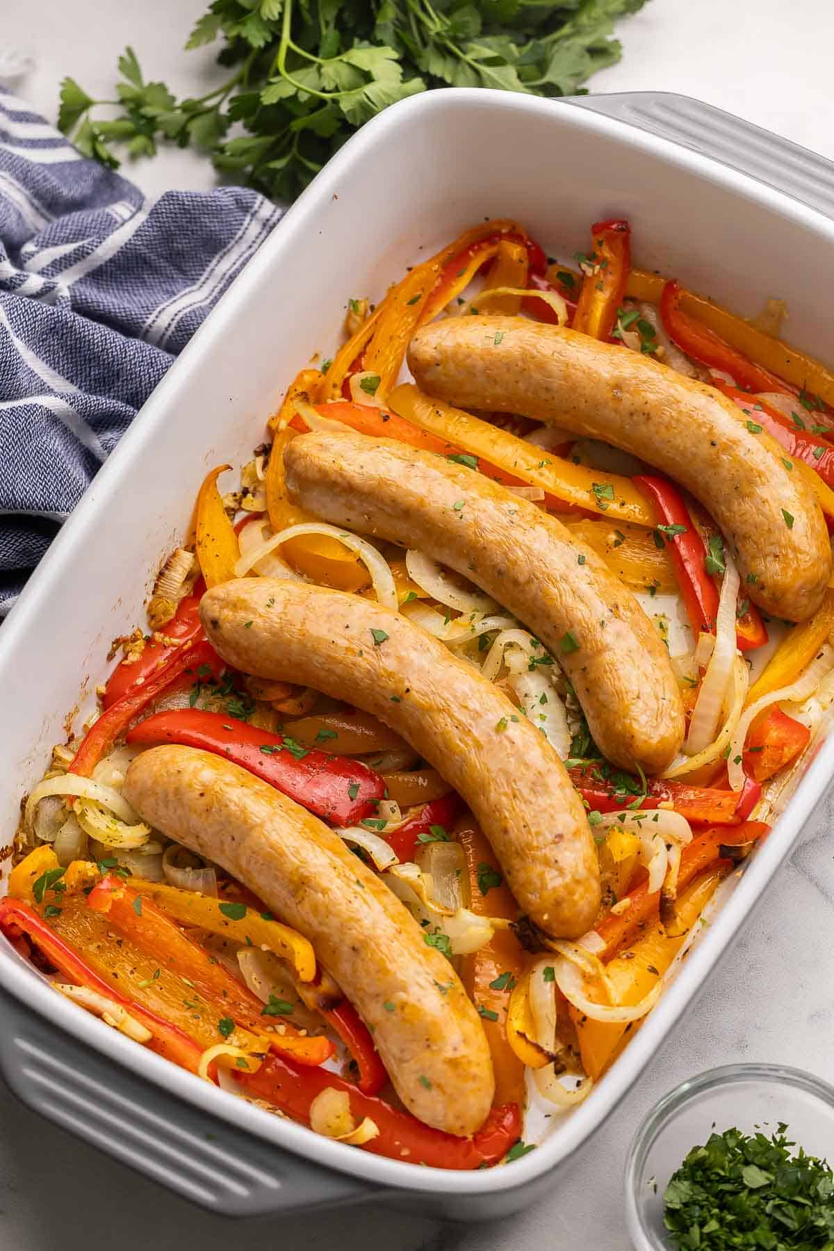 This Baked Sausage and Peppers practically cooks itself! Made with juicy Italian sausage, simple seasonings and sweet bell peppers, and ready in 35 minutes. #dinner #recipe | easy recipes | easy dinner ideas | italian sausage | one pan meal | comfort food | quick meals four sausages with peppers in a white and grey baking dish.