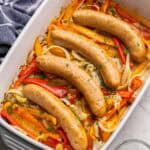 baked sausage and peppers in a white and grey baking dish.