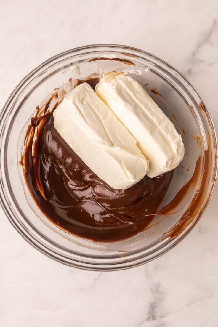 two blocks of cream cheese added to bowl of chocolate.