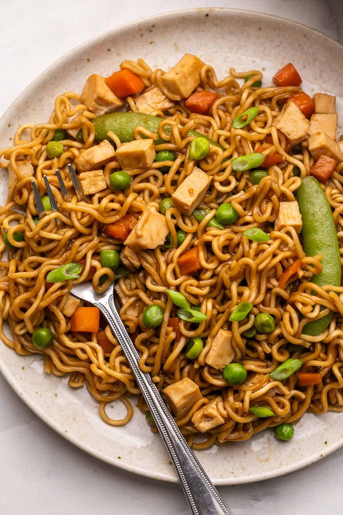 This Teriyaki Chicken Ramen Bake is a quick and easy 30-minute dinner with ramen noodles, tender cooked chicken breast, frozen veggies, and a sweet-savory sauce baked in one casserole dish! It's kid-friendly, customizable, and perfect for busy weeknights. #chicken #dinner | easy dinner ideas | chicken breast recipes | quick meals | easy recipes a fork in a plateful of teriyaki chicken ramen bake.