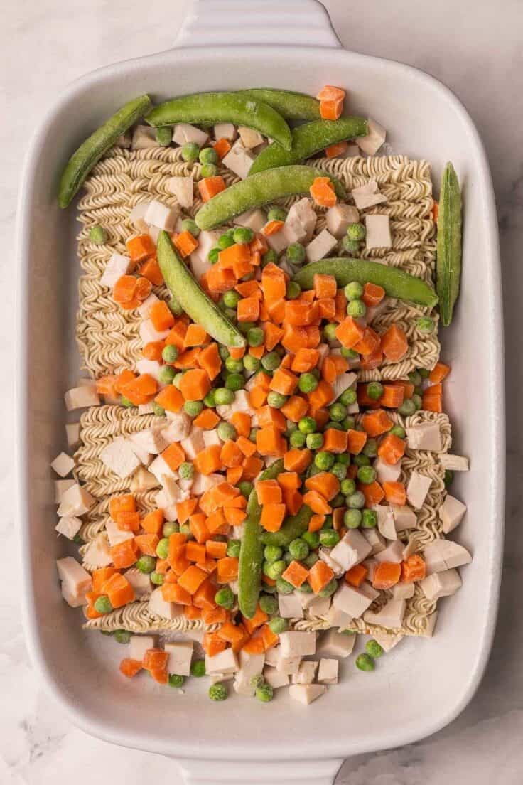 frozen peas and carrots added to noodles in white dish.
