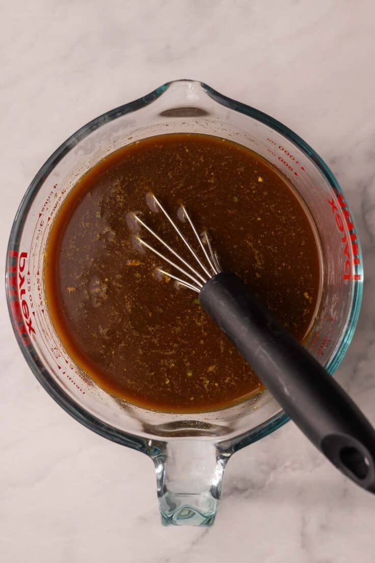 glass measuring cup with sauce and whisk.