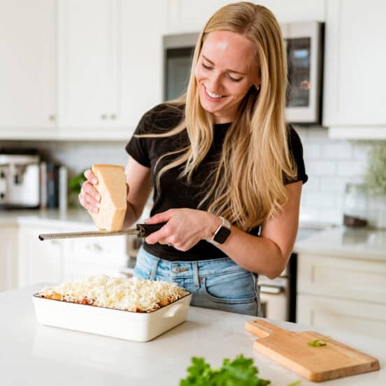 Ashley standing in a white kitchen grating cheese.