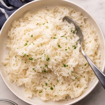 a spoon in bowl full of rice topped with chopped parsley.