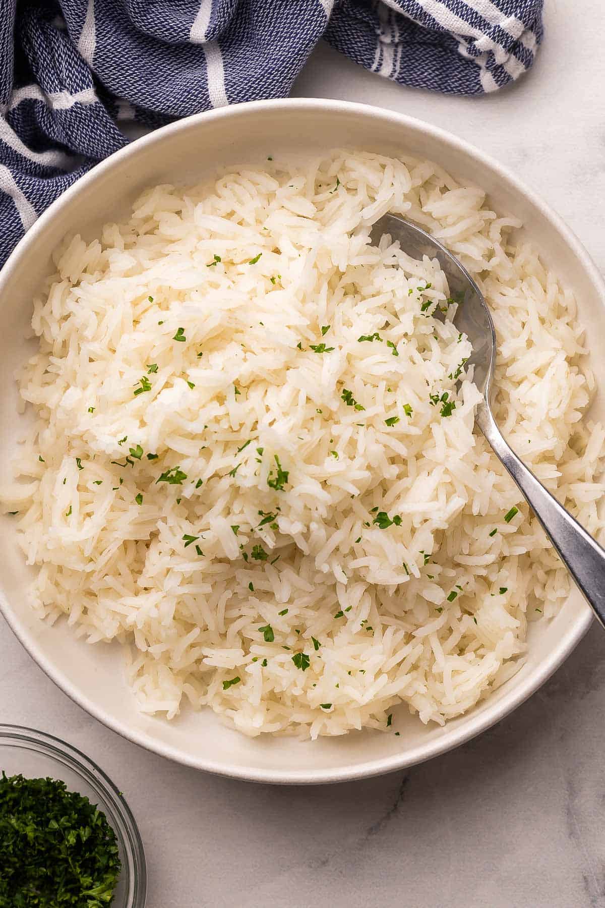 This Perfect Basmati Rice recipe is light, fluffy and never sticky! It takes just 20 minutes and comes out beautifully every single time. #rice #recipe #dinner | dinner recipes | easy recipes | how to cook rice | how to make rice | how to cook basmati rice | basmati rice recipe overhead image of basmati rice in a white bowl with a spoon.