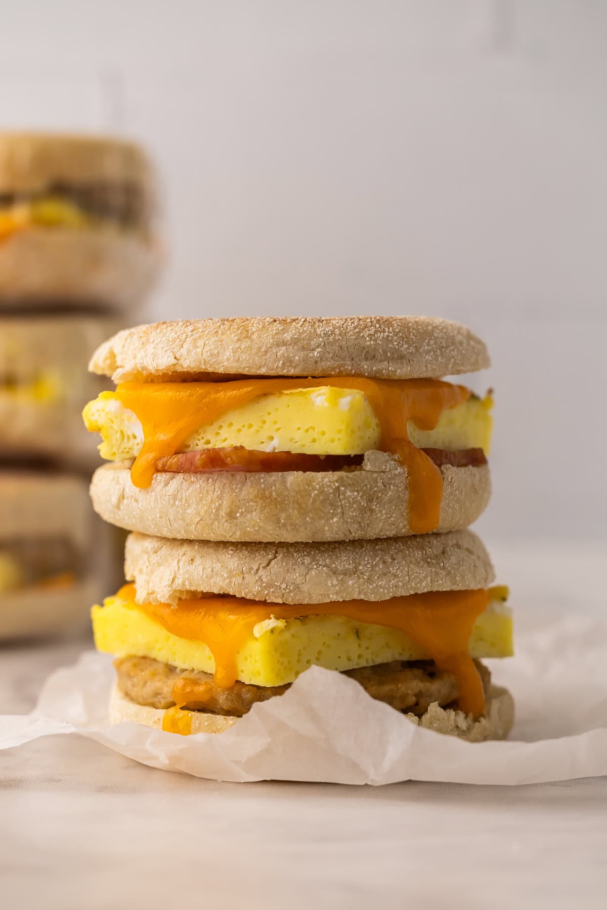These Make Ahead Freezer Breakfast Sandwiches are hearty, cheesy, and freezer-friendly. Made with egg, cheese and your choice of meat, they're perfect for busy mornings, meal prep, or road trips! #freezermeal #breakfast #recipe | breakfast sandwich | freezer meals | breakfast prep | eggs | sausage | bacon | high protein two breakfast sandwiches with melted cheese running down the side.
