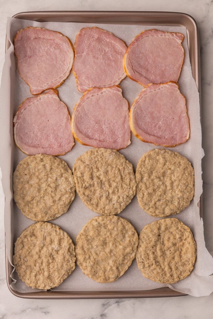 large pan lined with parchment filled with canadian bacon and sausage patties.