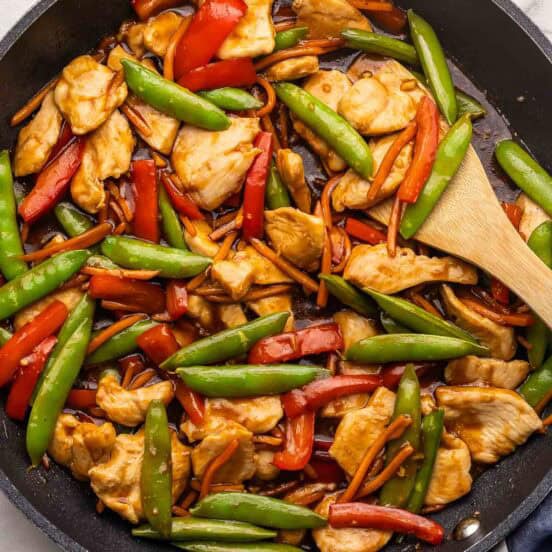 chicken stirfry with vegetables in a black skillet with wooden spoon.