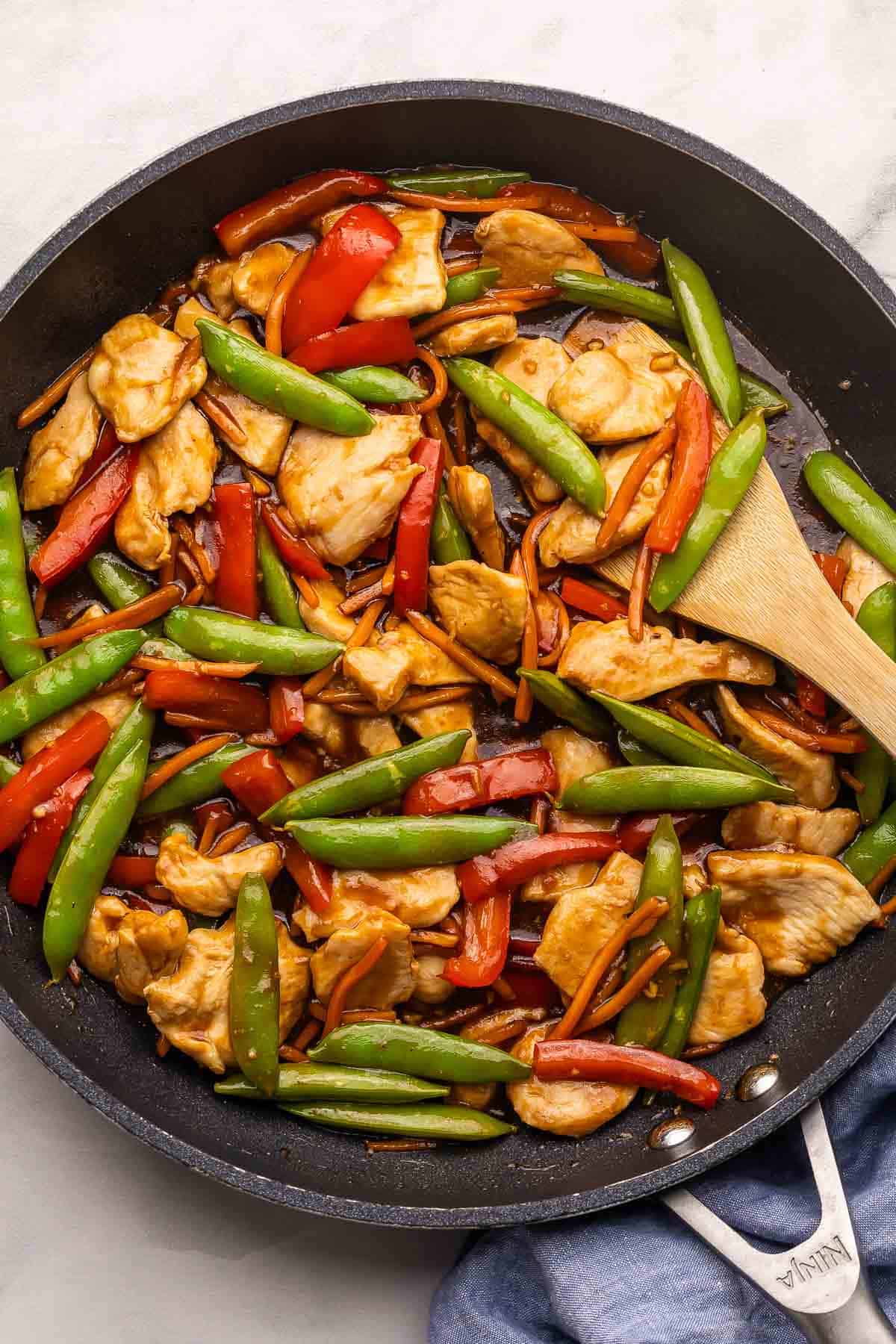chicken stirfry with vegetables in a black skillet with wooden spoon.