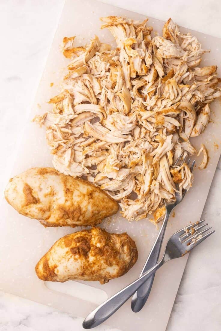 cooked taco chicken being shredded on a cutting board.