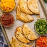 crispy baked chicken tacos on a pan with toppings beside.