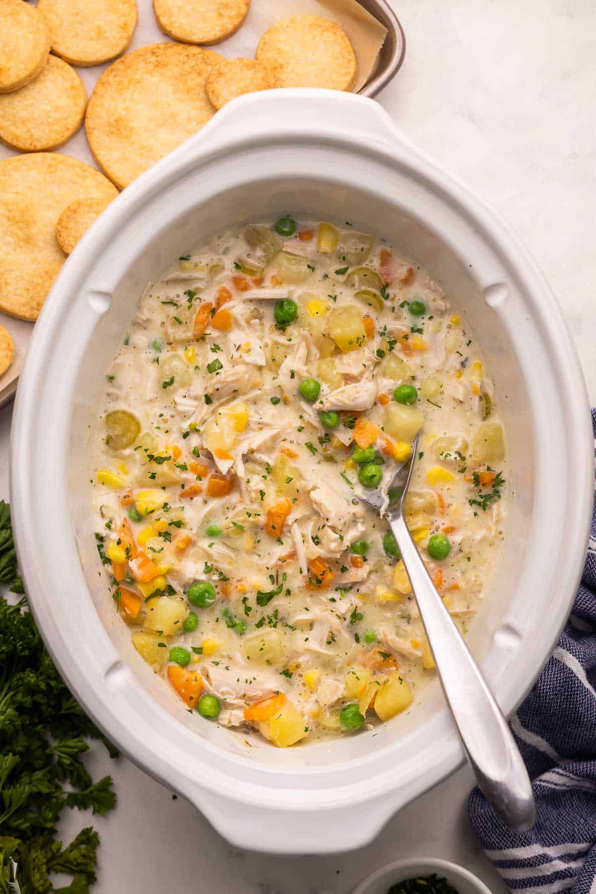 This Crockpot Chicken Pot Pie is loaded with tender chicken and vegetables in a creamy gravy and topped with golden pie crust rounds. A comforting slow cooker dinner with just 20 minutes of prep! #slowcooker #crockpot #dinner #recipe | slow cooker recipes | crockpot meals | slow cooker dinner | chicken recipes | chicken dinners | chicken breast | comfort food | dinner ideas a crockpot full of chicken pot pie with biscuits beside.