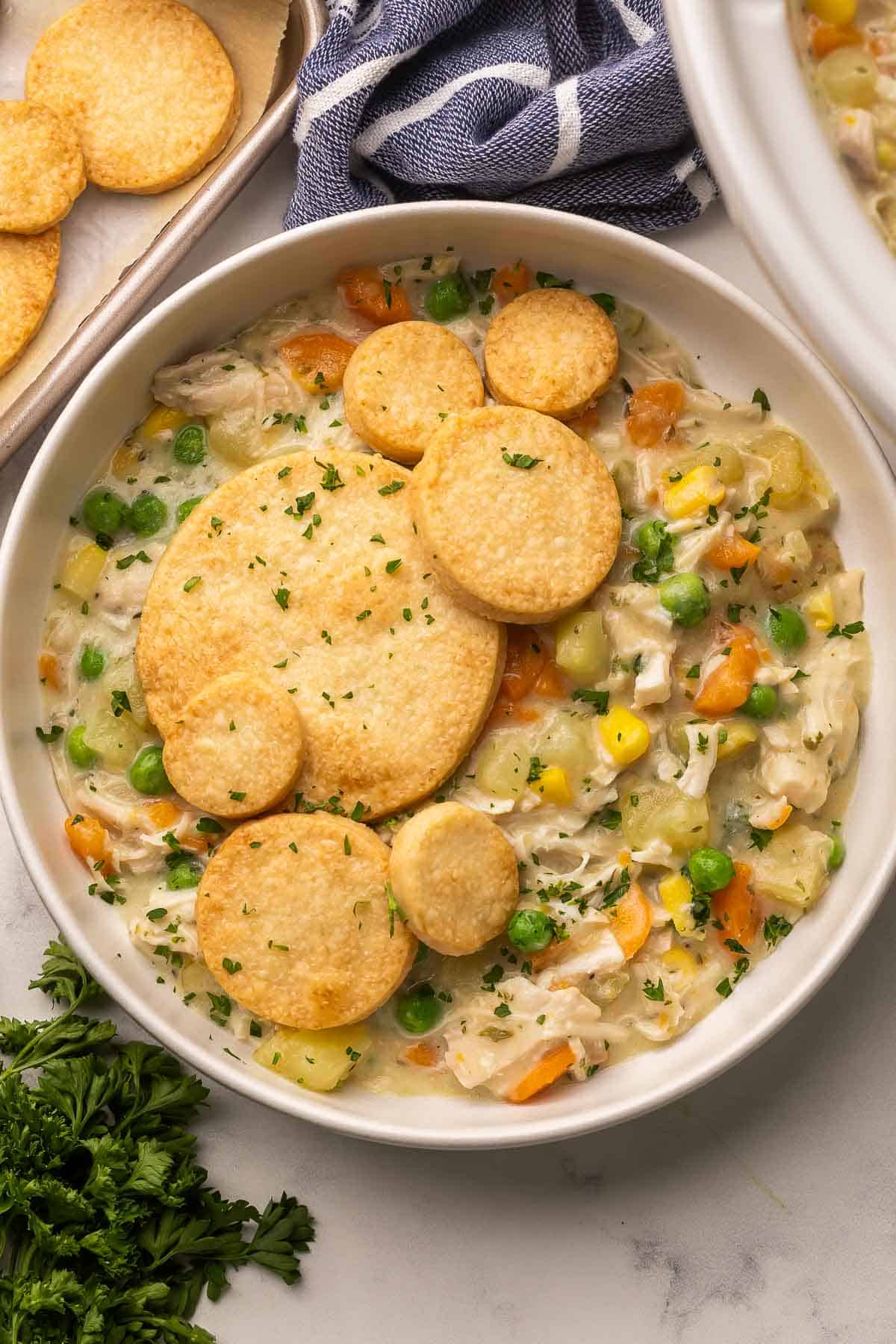 This Crockpot Chicken Pot Pie is loaded with tender chicken and vegetables in a creamy gravy and topped with golden pie crust rounds. A comforting slow cooker dinner with just 20 minutes of prep! #slowcooker #crockpot #dinner #recipe | slow cooker recipes | crockpot meals | slow cooker dinner | chicken recipes | chicken dinners | chicken breast | comfort food | dinner ideas biscuits on top of a bowl full of chicken pot pie.