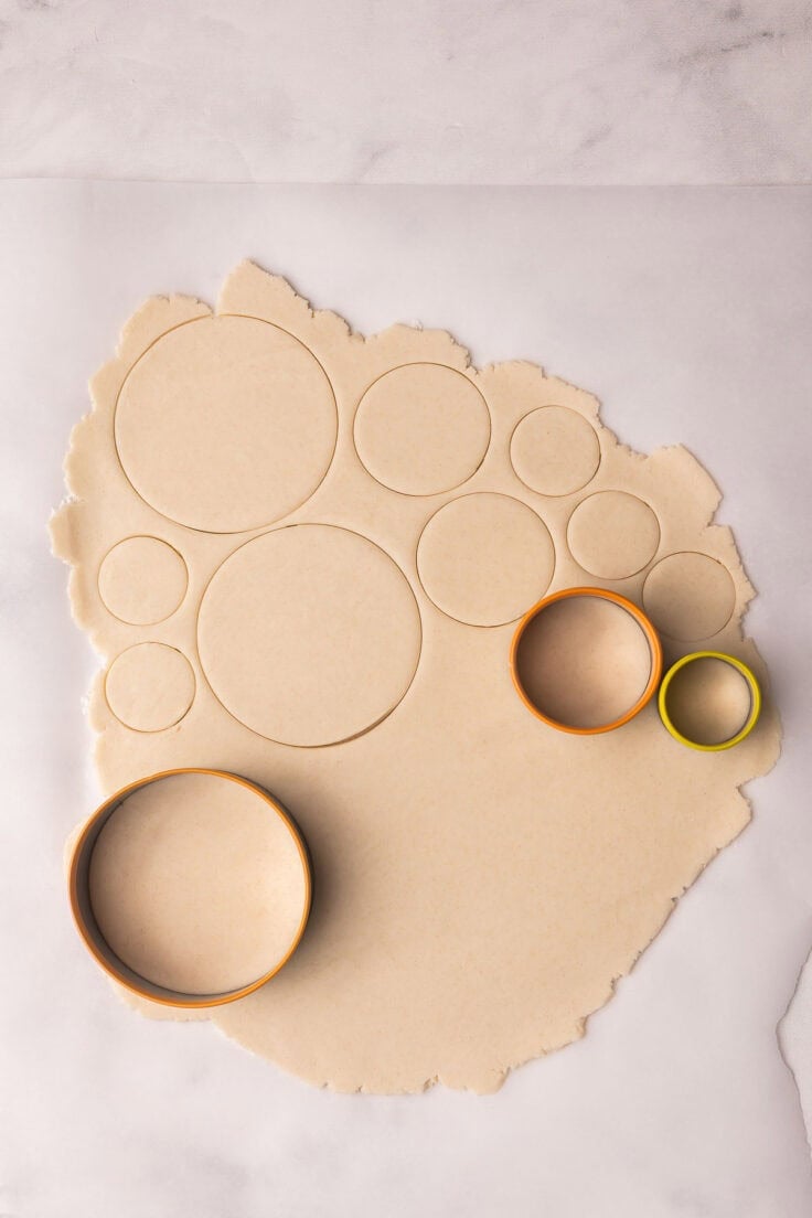 dough rolled flat with cookie cutters cutting out circles in the dough.