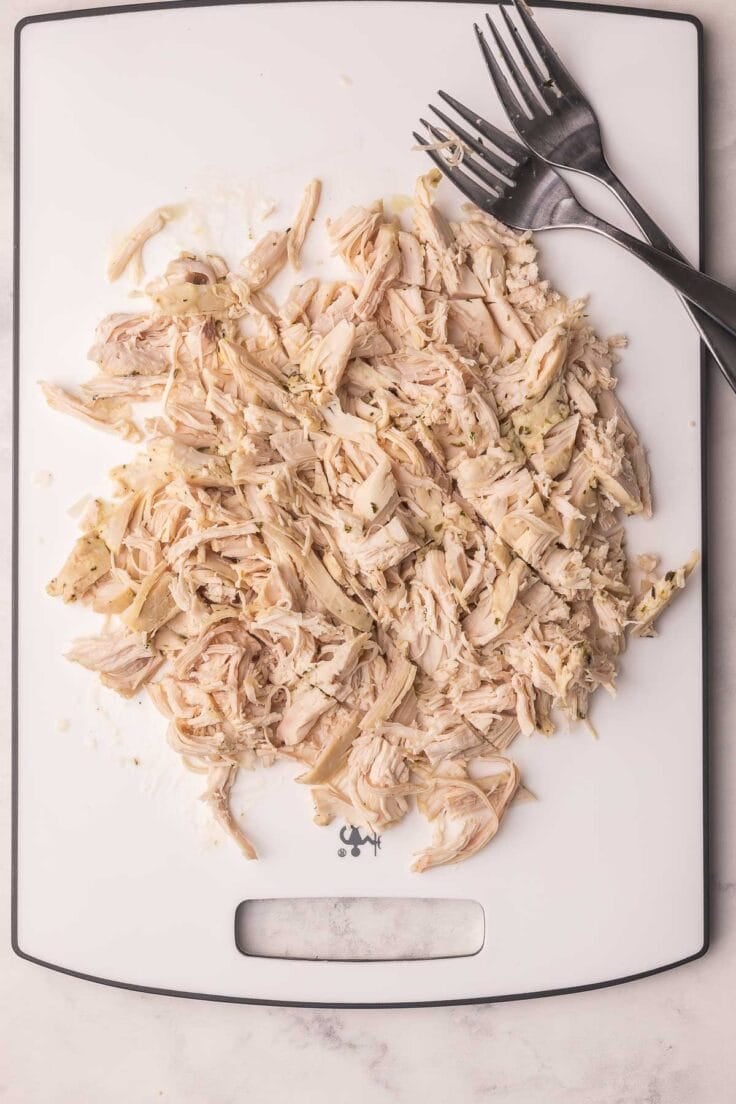 shredded chicken on a white cutting board with two forks.