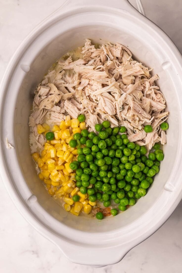 shredded chicken and vegetables added to white crockpot.